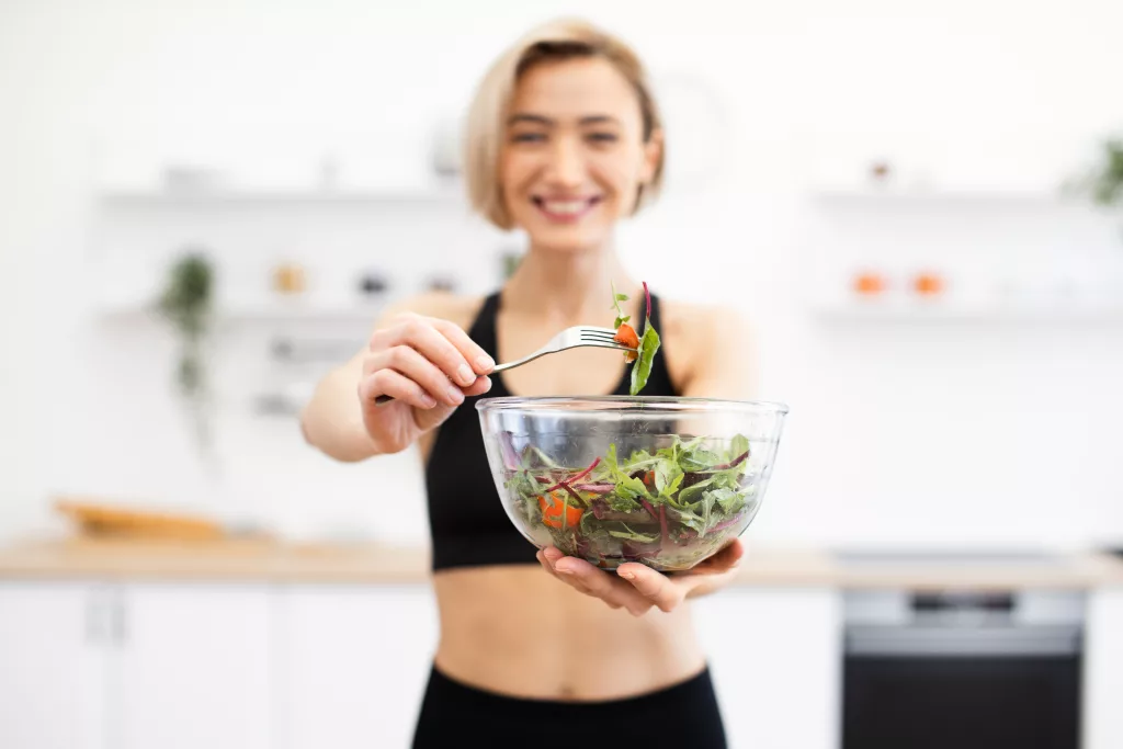 Uśmiechnięta kobieta trzymająca szklaną miskę ze świeżą sałatką w nowoczesnej kuchni